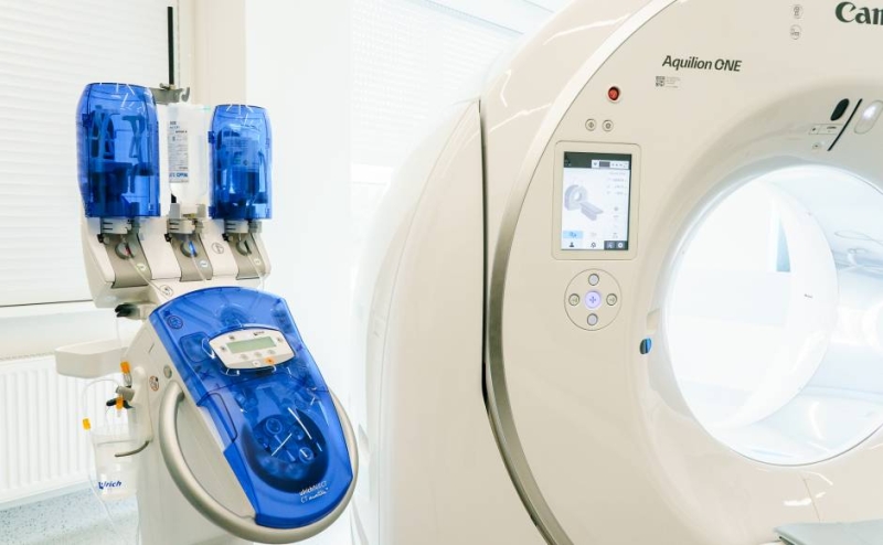 Canon Aquilion ONE datortomogrāfa tuvplāns ar kontrastvielas ievadīšanas medicīnisko injektoru līdzās.