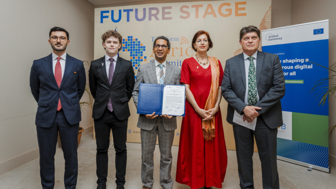 Pieci cilvēki stāv kopā pie sienas ar uzrakstu “Future Stage” un “Transform Africa Summit 2025”, viens tur atvērtu dokumentu mapē. Labajā pusē redzams plakāts ar Eiropas Savienības logotipu un tekstu par digitālās nākotnes veidošanu