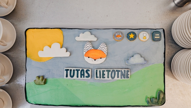 Bērnu pasākuma tematiskā kūka ar lapsas attēlu, sauli, mākoņiem un uzrakstu “Tutas lietotne”.