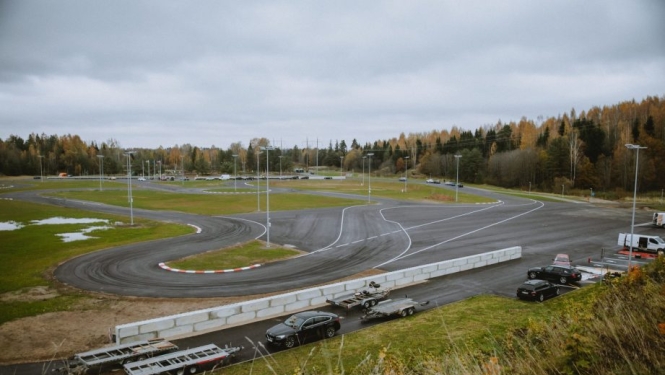 Plašs asfaltēts autosporta un braukšanas mācību laukums ar līkumiem un ceļa marķējumu, ko ieskauj rudens ainava.