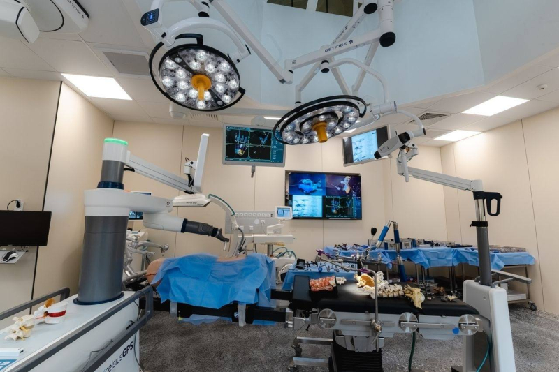 Moderna operāciju zāle ar augsti attīstītu medicīnisko tehnoloģiju – griestos uzstādīti divi lieli ķirurģiskie apgaismojuma lukturi, vairāki monitori rāda medicīniskos attēlus un datus, operāciju galds pārklāts ar zilām steriliem pārklājiem, apkārt izvietots dažāds medicīniskais aprīkojums un instrumenti. Telpa ir tīra un sakārtota, gatava sarežģītām ķirurģiskām procedūrām