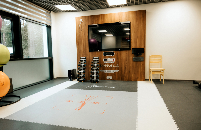 Treniņu zona ar vingrošanas paklājiem, sienas treniņu sistēmu ar ekrānu, hantelēm un koka apdari.