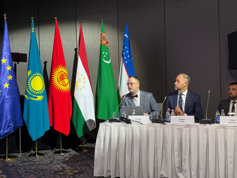 Starptautiska konference ar vairāku valstu karogiem fonā, tostarp Eiropas Savienības, Kazahstānas, Kirgizstānas, Tadžikistānas, Turkmenistānas un Uzbekistānas karogiem. Pie galda ar mikrofonu un vārdu kartītēm sēž trīs dalībnieki, uz galda redzamas ūdens pudeles un dokumenti