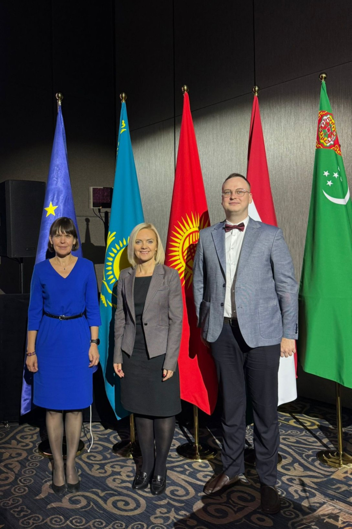Trīs personas formālā apģērbā stāv piecu karogu priekšā: Eiropas Savienības, Kazahstānas, Kirgizstānas, sarkanbalta karoga un Turkmenistānas karoga. Attēls uzņemts starptautiska pasākuma vai konferences laikā