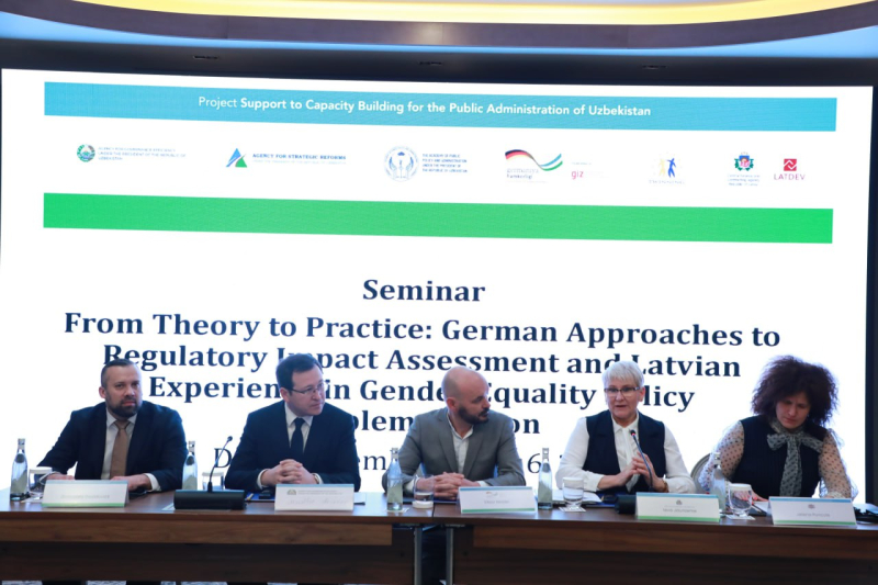 Piecu cilvēku paneļdiskusija seminārā “From Theory to Practice: German Approaches to Regulatory Impact Assessment and Latvian Experience in Gender Equality Policy Implementation”; fonā redzams liels ekrāns ar semināra nosaukumu un partneru logotipiem.