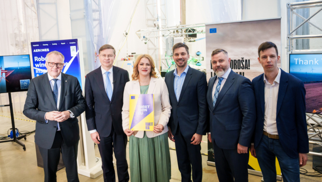 Industriālā vidē rindā sastājušies pieci vīrieši un viena sieviete, skatās kamerā un smaida. Sievietei rokās ir dokumentu mape