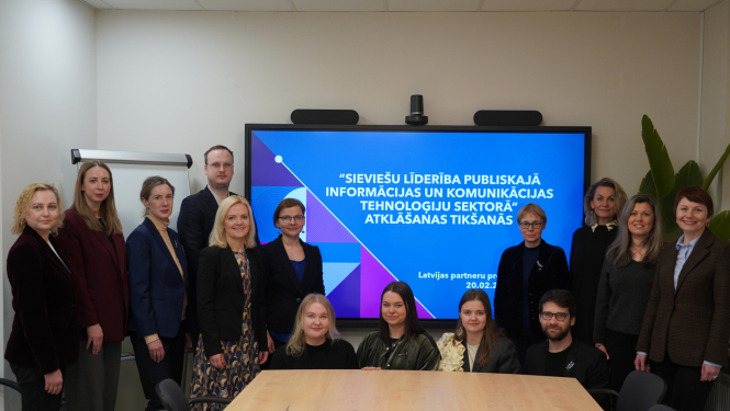 Grupas foto sanāksmē pie prezentāciju ekrāna, uz kura redzams pasākuma nosaukums “Sieviešu līderība publiskajā informācijas un komunikācijas tehnoloģiju sektorā” atklāšanas tikšanās. Dalībnieki nostājušies rindā ekrāna priekšā, fonā redzama tāfele un telpas interjers