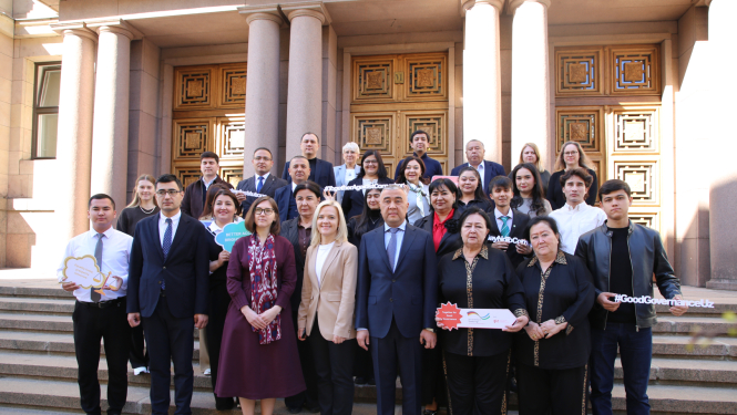 Grupas foto ar vairāk nekā 20 cilvēkiem, kas stāv uz kāpnēm pie monumentālas ēkas ar kolonnām un ornamentētām durvīm. 