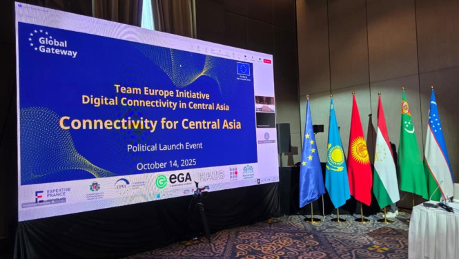 Konferences telpa ar lielu ekrānu, uz kura redzams uzraksts: ‘Global Gateway – Team Europe Initiative – Digital Connectivity in Central Asia – Political Launch Event – October 14, 2025’. Zem teksta izvietoti organizāciju logotipi, tostarp Expertise France, EGA un HAUS. Labajā pusē redzami vairāku valstu karogi: Eiropas Savienības, Kazahstānas, Kirgizstānas, Tadžikistānas, Turkmenistānas un Uzbekistānas