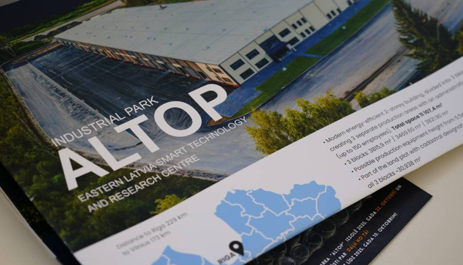 Brošūra par industriālo parku ALTOP Austrumlatvijā. Attēlā redzams liels rūpniecības ēku komplekss ar plašu autostāvvietu un zaļo zonu. Brošūras teksts norāda, ka ALTOP ir viedās tehnoloģijas un pētniecības centrs. Apakšējā daļā redzama karte ar attālumiem līdz Rīgai (224 km) un Viļņai (173 km).