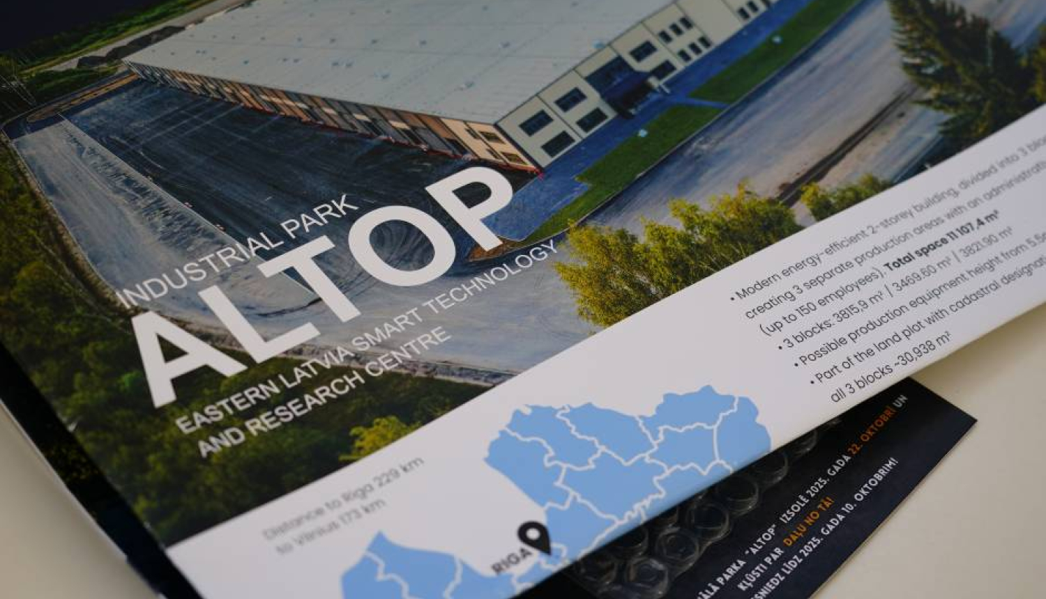 Brošūra par industriālo parku ALTOP Austrumlatvijā. Attēlā redzams liels rūpniecības ēku komplekss ar plašu autostāvvietu un zaļo zonu. Brošūras teksts norāda, ka ALTOP ir viedās tehnoloģijas un pētniecības centrs. Apakšējā daļā redzama karte ar attālumiem līdz Rīgai (224 km) un Viļņai (173 km).